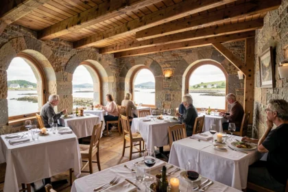 Salle de restaurant typique du Morbihan avec murs en pierre, poutres apparentes et tables dressées avec soin, vue sur un estuaire breton